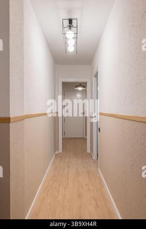 Innenkorridor mit Holzfußboden, weißen Türen, strukturierten beigefarbenen Wänden und Deckenleuchten in linearer Anordnung Stockfoto