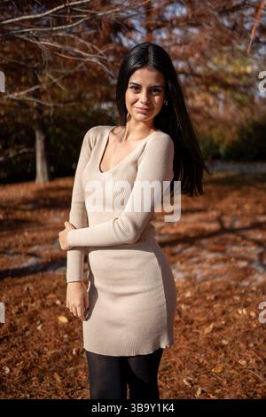 Modische junge Frau, die einen sonnigen Herbsttag in einem Park genießt, in einem stilvollen beigefarbenen Kleid und einer schwarzen Strumpfhose Stockfoto