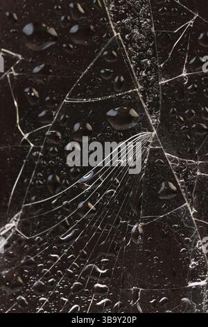 Wassertröpfchen bedeckt mit zerbrochenem Glas mit viel Beschädigung auf schwarzem Hintergrund, nasses, dünnes Glas in viele Stücke gebrochen, Nahaufnahme Stockfoto