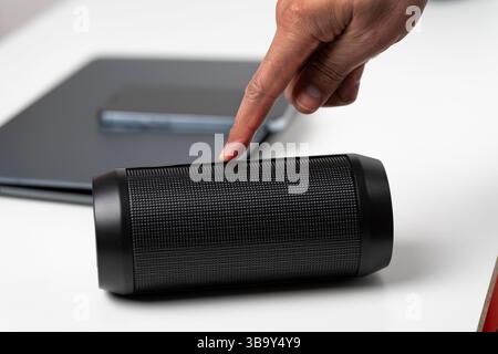 Nahaufnahme einer männlichen Hand, die zu Hause einen tragbaren roten Lautsprecher anschließt.Geschäftsmann genießt seine Lieblingsmusik, während er durch sein Smartphone scrollt.Techno Stockfoto