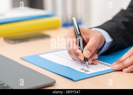 Nahaufnahme eines Geschäftsmannes, der den Bankscheck ausfüllt, der auf einem Schreibtisch im Büro sitzt Stockfoto