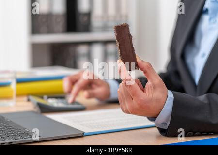 Nahaufnahme der Hände eines Geschäftsmannes, der Schokolade hält und im Büro arbeitet Stockfoto