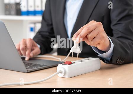 Nahaufnahme eines Mannes, der den Stecker an einer Steckdosenleiste mit einem Laptop auf einem Schreibtisch im Büro steckte Stockfoto