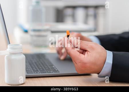 Nahaufnahme der Hand eines Geschäftsmannes mit Laptop, der Omega-Vitaminpille im Büro zeigt. Stockfoto