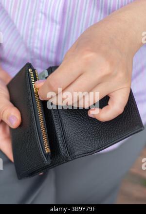 Nahaufnahme einer Person, die eine schwarze Ledertasche mit Reißverschluss öffnet. Die Person nutzt beide Hände, um auf die Geldbörse zuzugreifen, was eine mögliche Nutzung aufzeigt Stockfoto