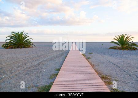 Hölzerne Terrassen in Form eines Pfads am Strand am Sonnenuntergang. Stockfoto