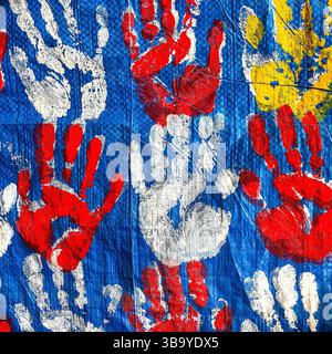 Handabdrücke des Künstlers mit roten, weißen und gelben Acrylfarben, die auf blaue Kunststofffolie aufgetragen werden. Stockfoto