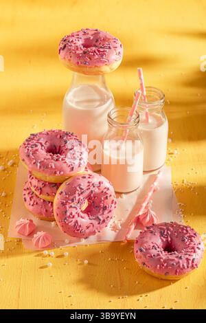 Leckere und frische rosa Donuts für Fat Thursday. Serviert mit Milch auf gelbem Tisch. Beliebtestes Dessert. Stockfoto