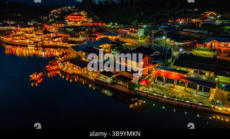 In der Abenddämmerung säumten die Lichter des Dorfes den See in chinesischen Strukturen mit farbenfrohen Lichtern. Ban Rak Thai ist Stockfoto