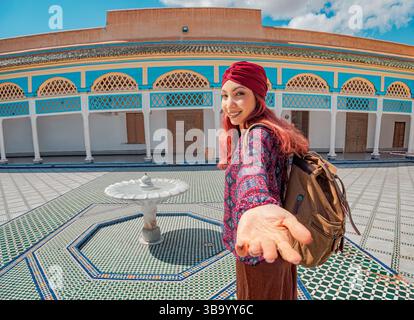 Junge Frau, lächelnd und streckt ihre Hand in der Follow Me Pose, während sie den lebhaften Bahia Palast in Marrakesch, Marokko, besucht Stockfoto