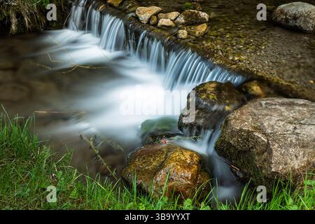 Blick auf einen kleinen Wasserfall in einem Gebirgsbach, umgeben von Felsen Stockfoto