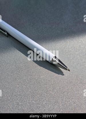 Ein weißer Kugelschreiber aus Metall, isoliert auf dem leuchtenden Hintergrund mit einem halben Sonnenlicht und Schatten. Die Macht eines Wissens. Stockfoto