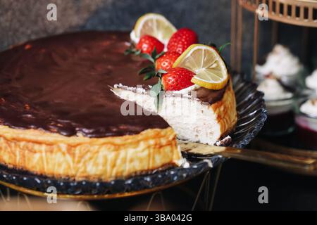 Schokoladen-Käsekuchen mit Früchten. Auf Dessertteller schneiden. Erdbeeren und Zitronengarnitur. Leckere hausgemachte süße Leckereien. Köstlicher gebackener Kuchen Stockfoto