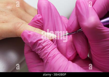 Nail Art im Gange. Feines Pinseldesign auf den Nägeln. Maniküre mit pinkfarbenen Handschuhen. Präzise Handmalerei. Schönheitssalon-Technik. Stockfoto