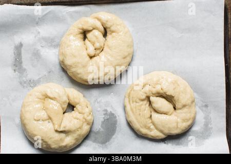 Blick von oben auf hausgemachten Brezelteig auf einem Backblech, Blick von oben auf frisch gekochten weichen Brezelteig auf weißem Hintergrund Stockfoto