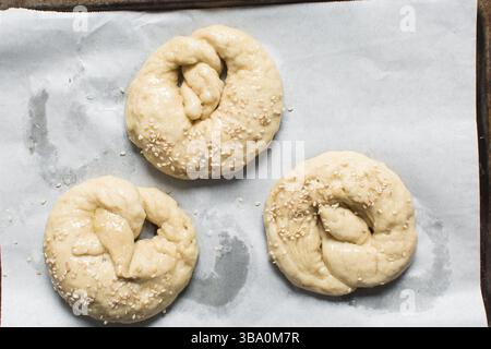 Blick von oben auf hausgemachten Brezelteig auf einem Backblech, Blick von oben auf frisch gekochten weichen Brezelteig auf weißem Hintergrund Stockfoto