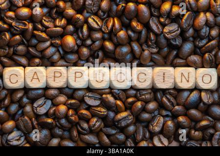 Hölzerne Buchstabenfliesen schreiben Cappuccino auf gerösteten Kaffeebohnen Hintergrund. Stockfoto