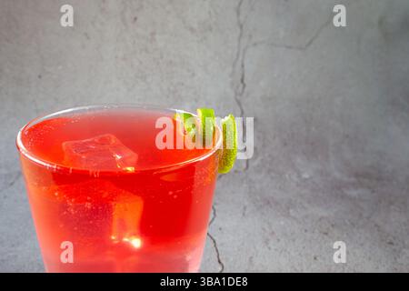 Ein Glas rotes Getränk mit einer Limettenscheibe darauf. Das Getränk wird in einem hohen Glas serviert, und die Limettenspirale wird auf der Flüssigkeit platziert. Konzept von Stockfoto