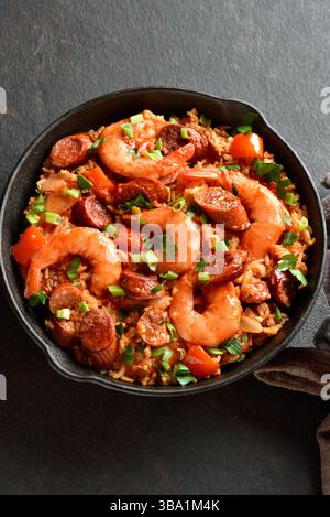 Kreolischer Jambalaya mit Garnelen, geräucherten Würstchen und Gemüse in gusseiserner Pfanne auf dunklem Hintergrund. Nahansicht Stockfoto