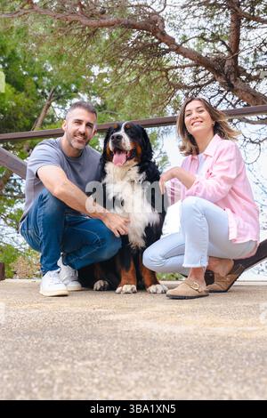 Ein lächelndes Paar mit Berner Sennenhund genießt im Frühling einen Moment im Freien Stockfoto