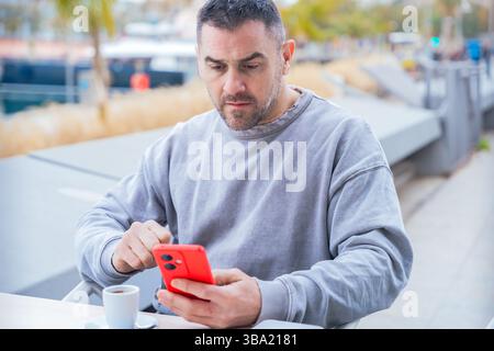 Ernsthafter Mann ernst, während er in einem Café im Freien auf ihrem Smartphone tippt. Stockfoto