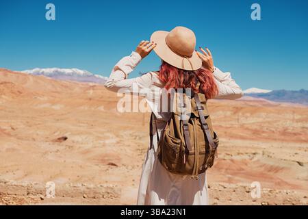 Weibliche Touristen mit Rucksack und Hut blicken auf eine weite Wüstenlandschaft mit schneebedeckten Bergen im Hintergrund Stockfoto