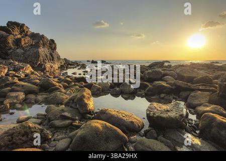 Runde Felsen und Kieselsteine, die bei Ebbe freigelegt werden, mit kleinen Meerespools bei Sonnenuntergang am Abend. Koh Lanta, Thailand, Asien Stockfoto