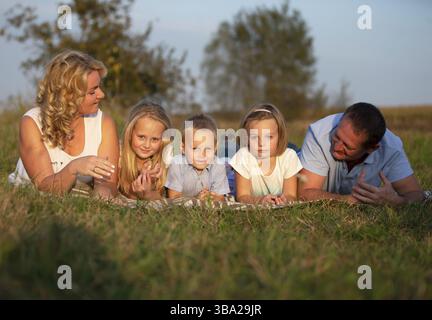 Glückliche Familie: Mutter, Vater, Kinder, Sohn und Töchter in der Natur. Eine schöne Familie liegt auf dem Gras im Park Stockfoto