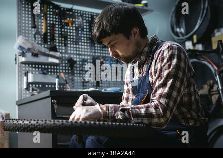 Junge kaukasische Werkstatt Reparatur Mountainbike Rad in Bike Shop Werkstatt. Fahrrad wird repariert. Pflege für Sie Räder. Mann Mechaniker arbeiten in der Garage. Stockfoto