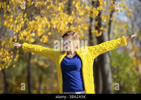 Schöne Frau freut sich an einem sonnigen Herbsttag, streut Ahornblätter, spaziert im Park Stockfoto