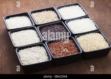 Verschiedene Reissorten in schwarzen Schüsseln auf Holztisch Stockfoto