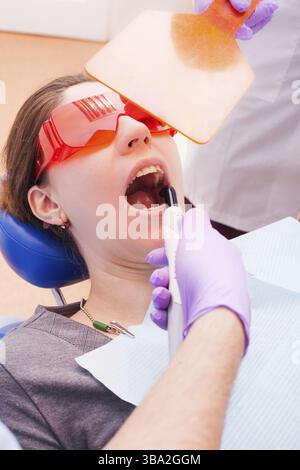 Der Patient liegt in speziellen Brillen zum Schutz gegen Laserstrahlen während der Zahnarzt mit Dental curing Light funktioniert Stockfoto
