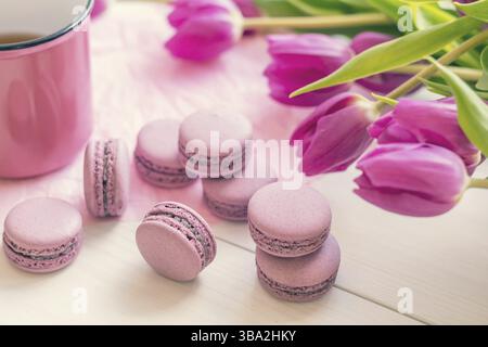 Violette süße köstliche Makronen und frische Tulpen auf weißem Hintergrund. Tasse heißer Tee. Geringe Schärfentiefe. Farbiges Foto Stockfoto