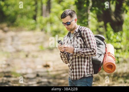 Hipster junger Mann mit Rucksack mit Smart Phone auf schöne Natur. Travel Concept. Outdoor reisen. Reisen und Entdecken. Backpacker männlichen Gehen in für Stockfoto