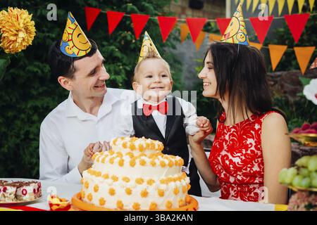 Kinder geburtstag Thema. Familie von drei kaukasischen Völker im Hinterhof des Hauses zu einem festlich dekorierten Tisch in lustigen Hüte und Kappen sitzen auf thei Stockfoto