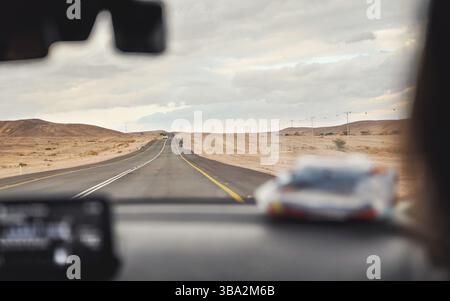 Auto fährt durch Wüstenlandschaft an bewölktem Tag, Blick vom Beifahrersitz, verschwommenes Armaturenbrett im Vordergrund, Roadtrip-Konzept, Israel, Asien Stockfoto