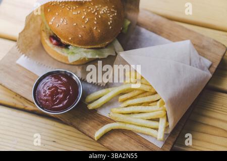 Frische leckere Burger und Pommes frites auf Holztisch. Pommes frites und BBQ Soße auf Holzplatte. Street Food Burger und Bratkartoffeln. Ungesunde Lebensmittel. Stockfoto