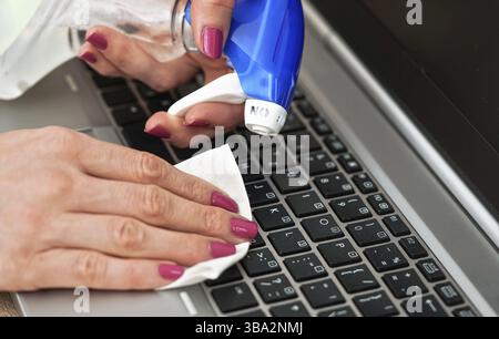 Frau, die Laptoptastatur mit weißem Tuch reinigt, Detail auf ihren Fingern, das Papiertuch hält, blauer Alkoholsprüher in der Nähe - Desinfektionskonzept, Liptovs Stockfoto