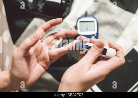 Thema Diabetes. Eine Nahaufnahme Makro planen. Die Hände eines jungen kaukasischen Frau zu Hause im Schlafzimmer auf dem Bett. Es nutzt die Technologie eines Instruments für Stockfoto