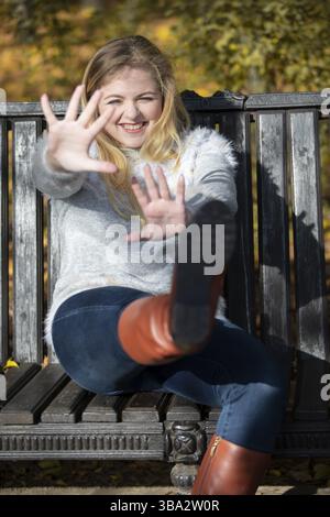 Schöne junge Frau in einem Herbstpark sitzt auf einer Bank Stockfoto