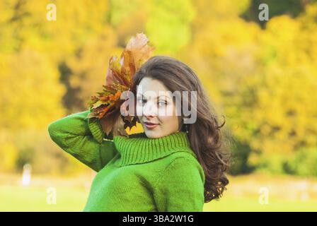 Beautiful brunette woman with maple leaves, autumnal background with copy space Stockfoto