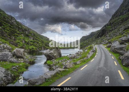Kurvenreiche Straße durch Gap of Dunloe mit Stone Wishing Bridge in der Ferne, Black Valley, MacGillycuddys Reeks Mountains, Ring of Kerry, Irland Stockfoto