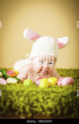 Drei Monate lang lag das Baby auf dem Bauch als Osterhase auf dem Gras mit Eiern Stockfoto