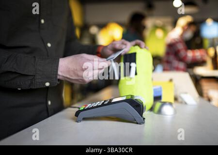 Der Verkäufer hält das Zahlungsterminal, während er den Beleg für den Abschluss des Kaufs hält. Nahaufnahme der Hände. Konzept von NFC, Geschäfts- und Bankgeschäften. Paym Stockfoto