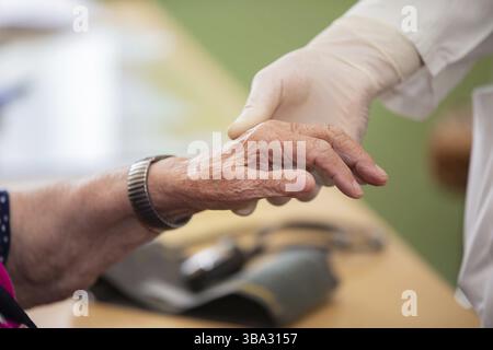 Die Hand des Doktors hält die Hand des alten Mannes. Nahaufnahme eines Arztes und die zitternde Hand einer behinderten älteren Frau. Das Konzept des menschlichen Alterns Stockfoto