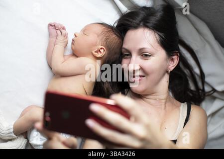 Nahaufnahme einer Mutter und ihres neugeborenen Babys, die ein Selfie oder einen Videoanruf mit ihrem Vater oder Verwandten im Bett machen. Technologiekonzept, neue Generation, Familie Stockfoto