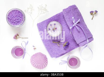 Spa-Produkte. Lavendelbadesalze, trockene Blumen, Seife, Kosmetikcreme, Kerzen und Handtuch. Violett-violett-Konzept. Flach auf weißem Hintergrund, Draufsicht Stockfoto