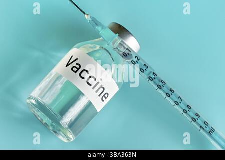 Glasfläschchen mit Label-Impfstoff und hypodermischer Spritzennadel in der Nähe, Ansicht von oben auf grünem cyanfarbenem Hintergrund Stockfoto
