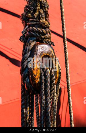 Abgenutzte Seile und hölzerne Öse auf einem Nachbau-Schiff mit rotem Holz im Hintergrund Stockfoto