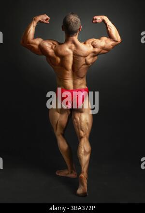 Junge bodybuilder Mann zurück gebogen Doppel bicpes darstellen, zeigen seine riesige trapezius, rhomben, levator, Latissimus dorsi und Beine Muskeln. Studio shot o Stockfoto